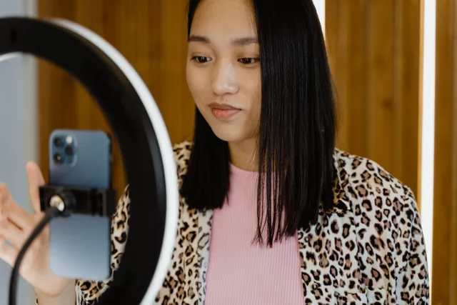 A young woman using a smartphone and ring light for video recording indoors. UGC creator platform fees: what each platform takes and what you keep