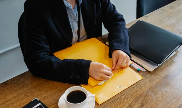 High angle of crop faceless female in formal clothes sitting at wooden table with coffee and documents while having break in workplace. UGC creator platform setup standard: document control, account access and escalation