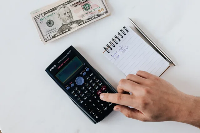 Top view of crop unrecognizable economist calculating on calculator on table with notepad and pen near pile of dollar banknotes on marble table. How to write a UGC creator business quote, with pricing examples